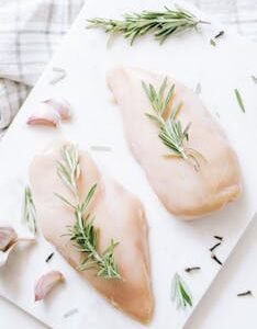 High-angle view of raw chicken breasts on marble with rosemary and garlic, ideal for healthy recipe inspiration.